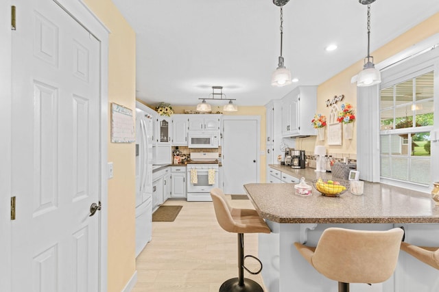 1850 E Farm Road 88, Springfield, MO 65803 - kitchen with white appliances, a peninsula, a breakfast bar, light wood-style floors, and decorative light fixtures
