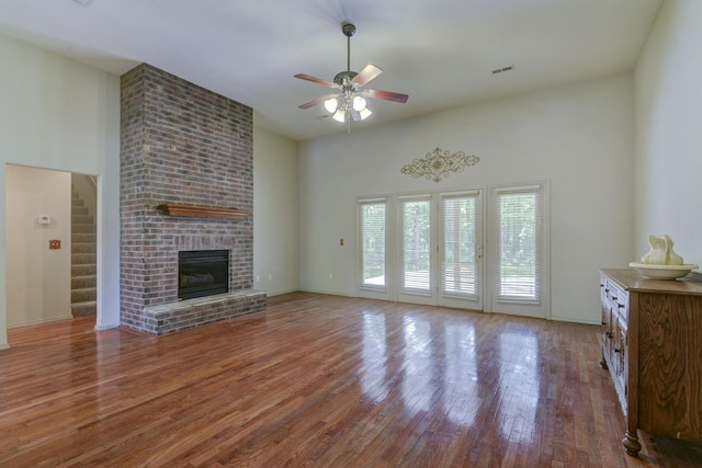 613 Crossing Dr, Branson West, MO 65737 - unfurnished living room with ceiling fan, wood finished floors, a towering ceiling, a brick fireplace, and stairway