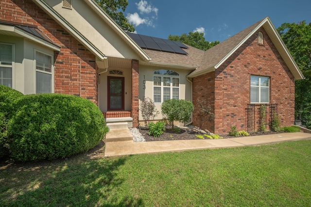 103 Fawn Trl, Neosho, MO 64850 - view of exterior entry featuring brick siding, roof mounted solar panels, a yard, and a shingled roof