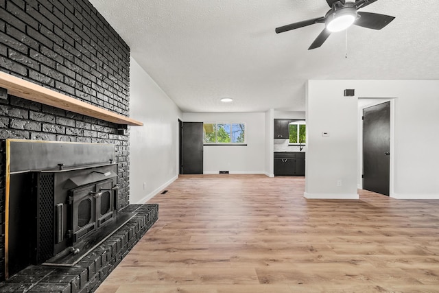 302 W Howard Ave, Billings, MO 65610 - unfurnished living room featuring a textured ceiling, light wood-style flooring, ceiling fan, and a wood stove