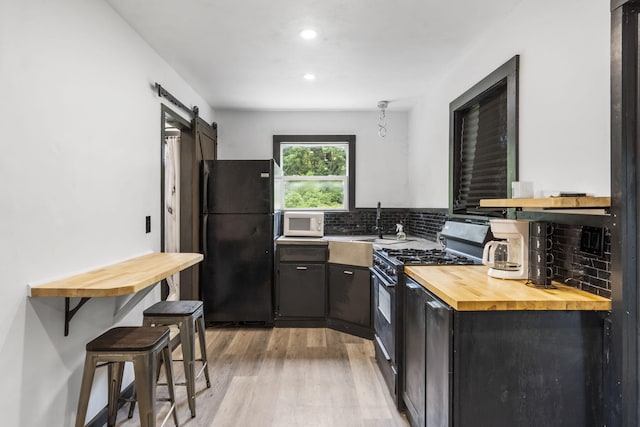 3430 S Elmview Ave, Springfield, MO 65804 - kitchen featuring black appliances, wood counters, light wood-type flooring, a barn door, and decorative backsplash