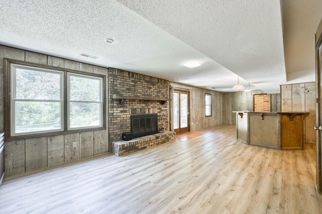 5751 S Kings Ave, Springfield, MO 65810 - unfurnished living room with light wood-type flooring, a textured ceiling, a fireplace, and wooden walls