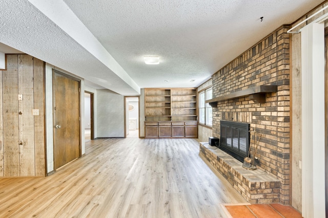 5751 S Kings Ave, Springfield, MO 65810 - unfurnished living room featuring a textured ceiling, light wood-style floors, built in features, a fireplace, and wood walls