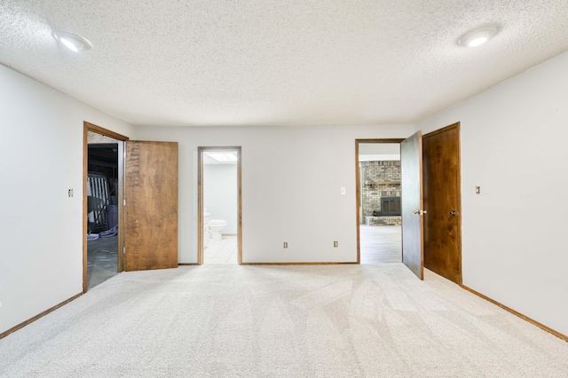 5751 S Kings Ave, Springfield, MO 65810 - unfurnished bedroom featuring a textured ceiling, ensuite bathroom, carpet flooring, a closet, and a brick fireplace