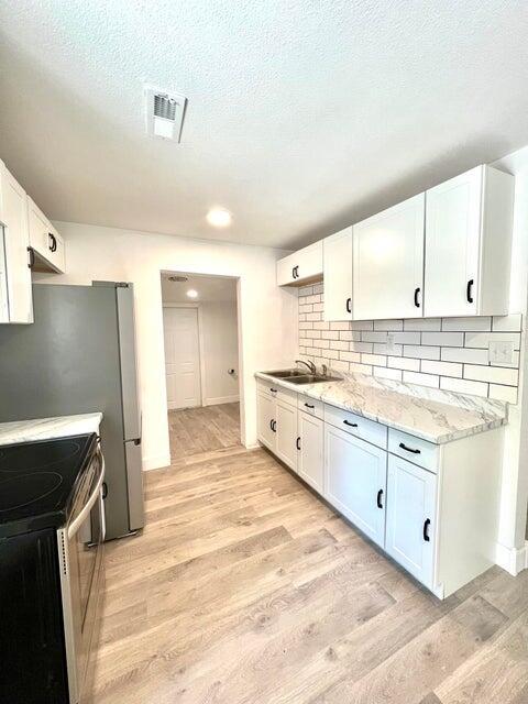 900 N Eagle Ave, Springfield, MO 65802 - kitchen with stainless steel electric range, light wood finished floors, tasteful backsplash, white cabinetry, and light stone counters