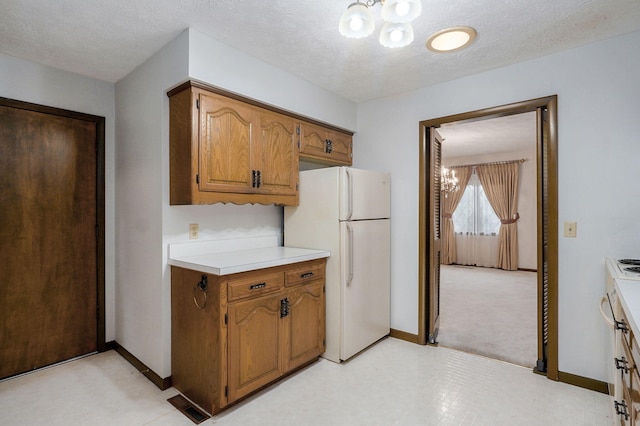 3520 E Carol Dr, Springfield, MO 65809 - kitchen with a chandelier, freestanding refrigerator, light countertops, brown cabinetry, and a textured ceiling