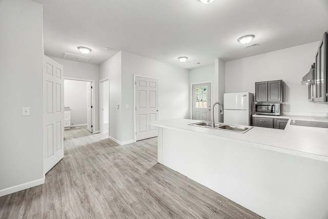 kitchen with freestanding refrigerator, light wood-style floors, stainless steel microwave, and light countertops