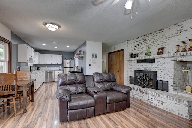 2148 Carrie St, Carthage, MO 64836 - living room featuring light wood finished floors, a textured ceiling, a brick fireplace, and ceiling fan