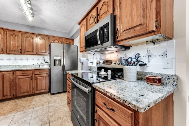 150 Sunken Forest Dr Unit 10-253, Forsyth, MO 65653 - kitchen with appliances with stainless steel finishes, brown cabinets, decorative backsplash, a textured ceiling, and light stone countertops