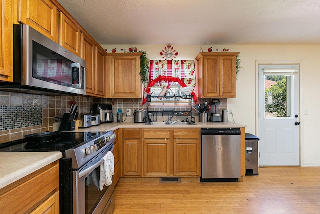 5441 Basswood Ct W, Springfield, MO 65802 - kitchen with appliances with stainless steel finishes, tasteful backsplash, light countertops, light wood finished floors, and brown cabinetry