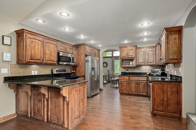623 E Weaver Rd, Springfield, MO 65810 - kitchen with stainless steel appliances, a peninsula, dark wood-style flooring, decorative backsplash, and arched walkways