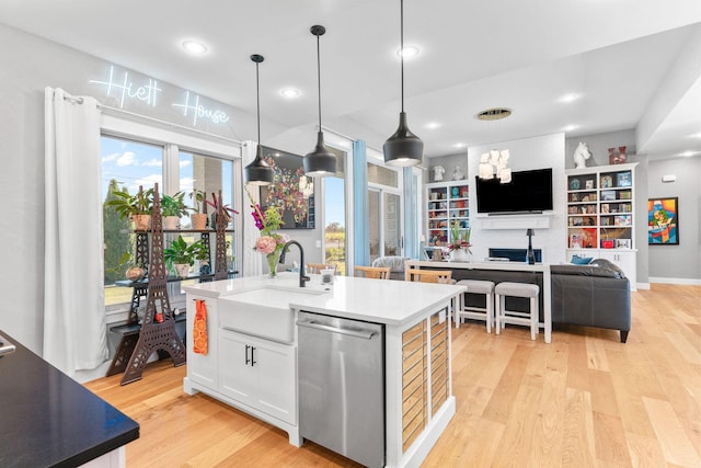3972 E Dunrobin Dr, Springfield, MO 65809 - kitchen with stainless steel dishwasher, light wood-style flooring, white cabinets, an island with sink, and decorative light fixtures
