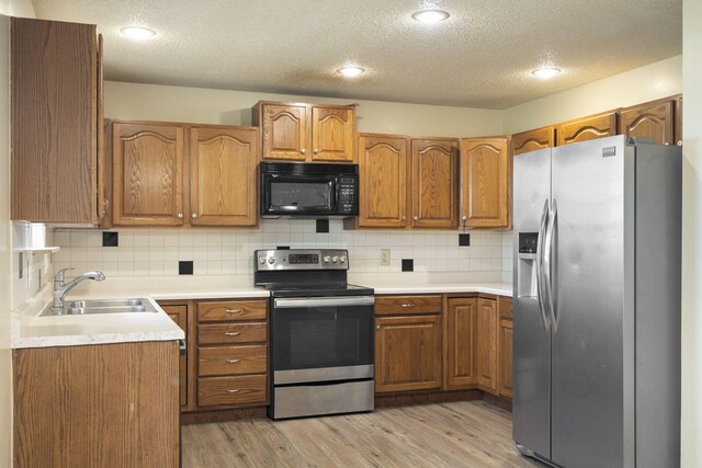 1813 Boswell Ave, Branson, MO 65616 - kitchen with stainless steel appliances, brown cabinetry, light wood-type flooring, a textured ceiling, and tasteful backsplash