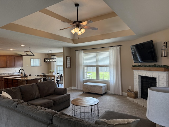 1129 S Erika Ave, Springfield, MO 65802 - living room with light carpet, a ceiling fan, a tray ceiling, and a brick fireplace