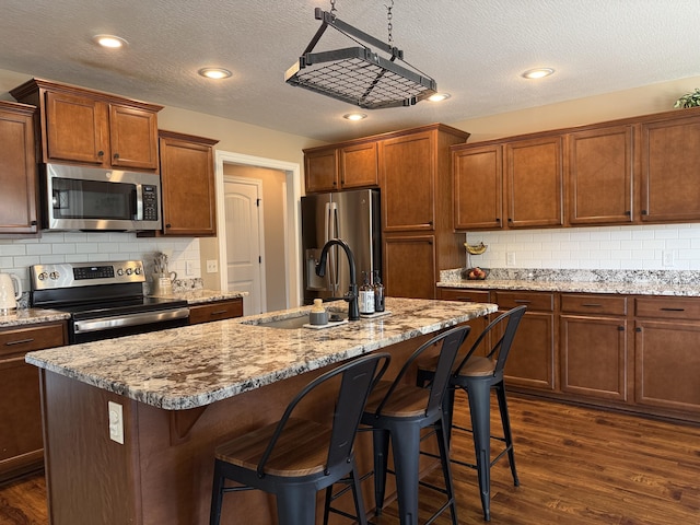 1129 S Erika Ave, Springfield, MO 65802 - kitchen featuring stainless steel appliances, dark wood finished floors, an island with sink, a kitchen breakfast bar, and a textured ceiling