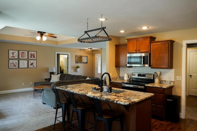 1129 S Erika Ave, Springfield, MO 65802 - kitchen featuring appliances with stainless steel finishes, open floor plan, a ceiling fan, light stone counters, and a kitchen island with sink