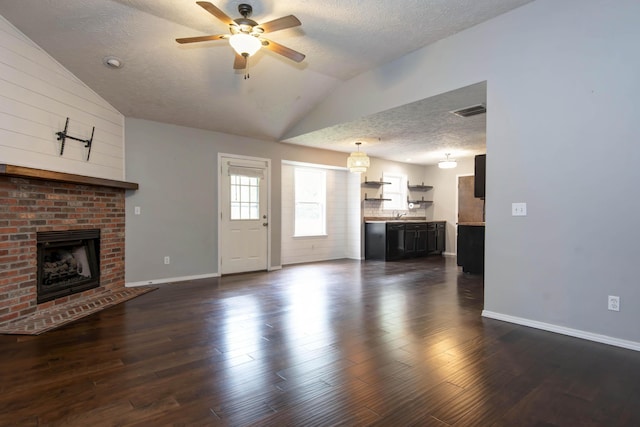 4252 W Madison St, Springfield, MO 65802 - unfurnished living room featuring vaulted ceiling, a textured ceiling, ceiling fan, a brick fireplace, and dark wood-type flooring