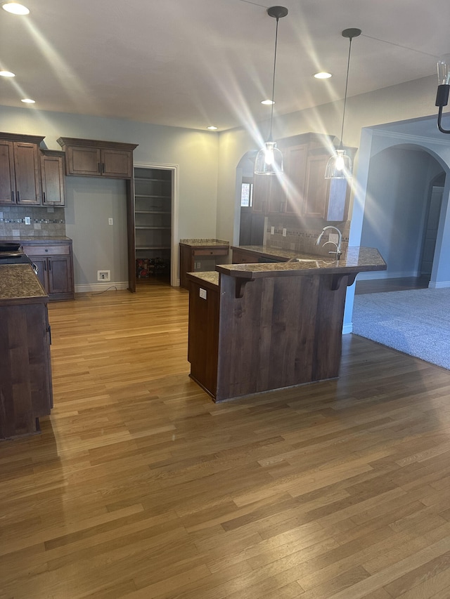 5605 N Seacrest Dr, Ozark, MO 65721 - kitchen featuring arched walkways, dark countertops, a breakfast bar, backsplash, and light wood finished floors