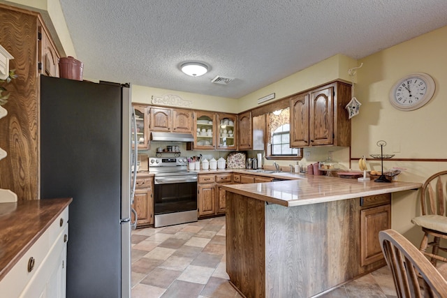 1706 Ankney Pl, Neosho, MO 64850 - kitchen with stainless steel appliances, a peninsula, under cabinet range hood, a kitchen bar, and brown cabinets