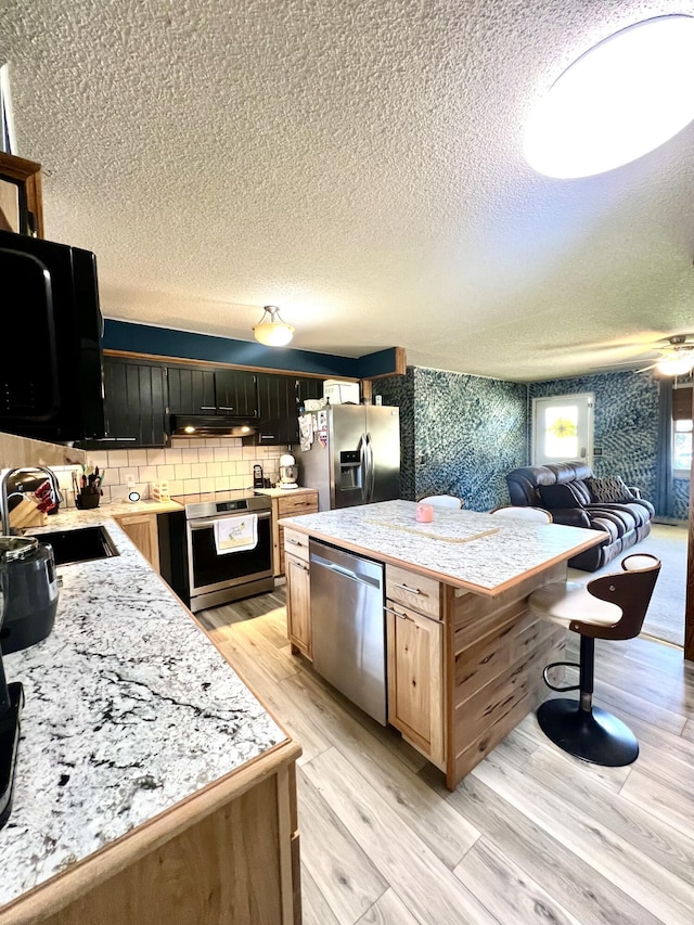817 Fillmore St, Mount Vernon, MO 65712 - kitchen featuring stainless steel appliances, under cabinet range hood, a center island, a textured ceiling, and open floor plan