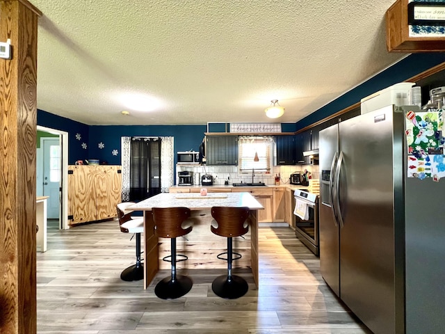 817 Fillmore St, Mount Vernon, MO 65712 - kitchen with appliances with stainless steel finishes, light countertops, light wood-style floors, a breakfast bar area, and a textured ceiling