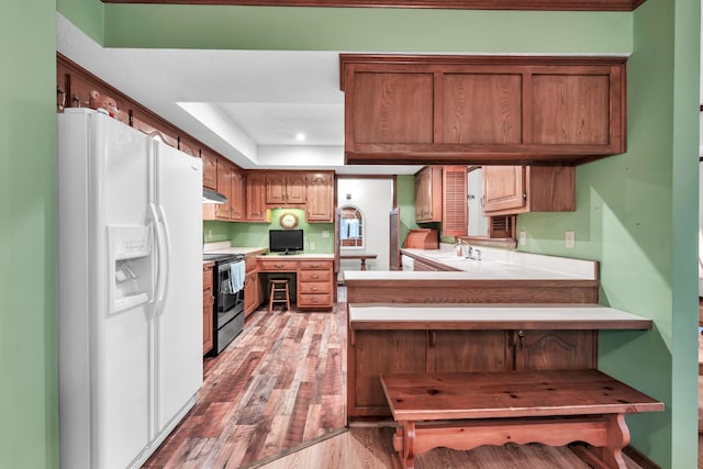 1011 W Tracy St, Springfield, MO 65807 - kitchen featuring white refrigerator with ice dispenser, stainless steel electric range oven, light wood-style flooring, under cabinet range hood, and a peninsula