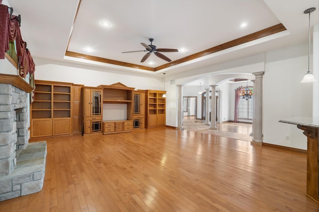 744 Seven Pines Dr, Saddlebrooke, MO 65630 - unfurnished living room with decorative columns, a tray ceiling, a ceiling fan, arched walkways, and a fireplace