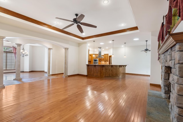 744 Seven Pines Dr, Saddlebrooke, MO 65630 - unfurnished living room with decorative columns, a ceiling fan, a tray ceiling, arched walkways, and light wood-style flooring