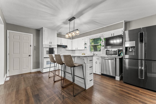 522 S Belcrest Ave, Springfield, MO 65802 - kitchen featuring appliances with stainless steel finishes, dark wood finished floors, under cabinet range hood, a chandelier, and white cabinetry