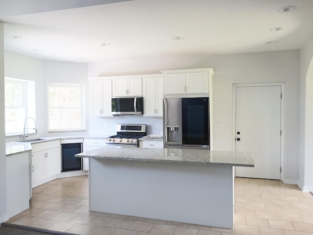 6540 Gateway Dr, Joplin, MO 64804 - kitchen featuring appliances with stainless steel finishes, beverage cooler, a center island, light stone countertops, and white cabinetry