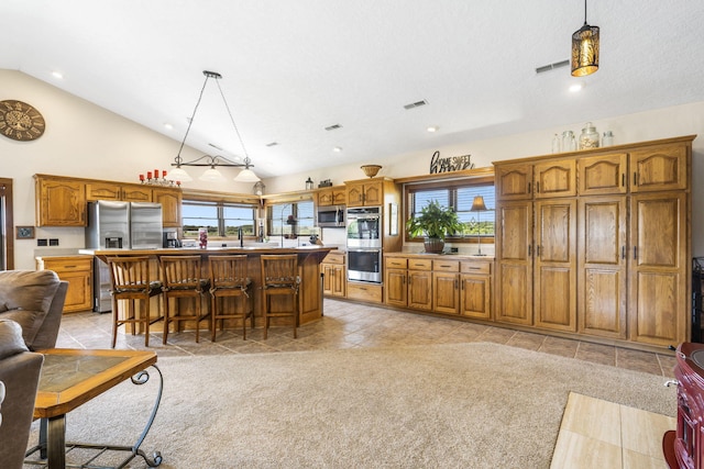 14410 Native Dr, Phillipsburg, MO 65722 - kitchen featuring stainless steel appliances, brown cabinets, open floor plan, vaulted ceiling, and pendant lighting
