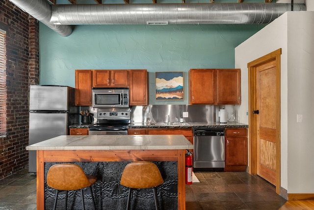 509 W Olive St Unit 206, Springfield, MO 65806 - kitchen with stainless steel appliances, brown cabinetry, dark stone finish flooring, brick wall, and a center island