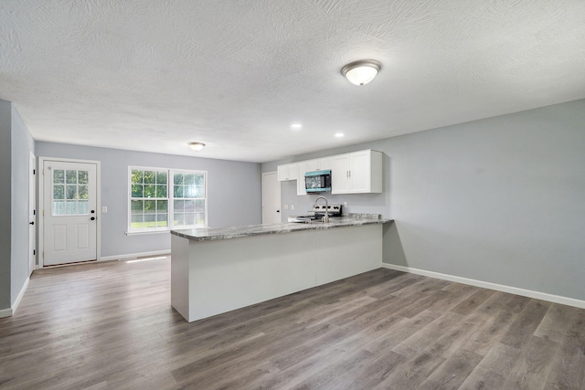 1020 Gretchen St, Nixa, MO 65714 - kitchen featuring stainless steel microwave, stove, a peninsula, white cabinetry, and dark wood-style flooring