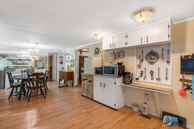 6665 State Highway 173, Cape Fair, MO 65624 - kitchen featuring stainless steel microwave, white cabinets, a chandelier, light wood-style floors, and freestanding refrigerator