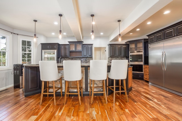 4225 E Crosswinds Pl, Springfield, MO 65809 - kitchen featuring appliances with stainless steel finishes, light wood-style flooring, backsplash, a kitchen bar, and a large island with sink