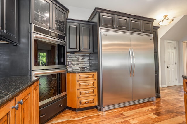 4225 E Crosswinds Pl, Springfield, MO 65809 - kitchen featuring stainless steel appliances, dark stone countertops, backsplash, glass insert cabinets, and light wood-style floors