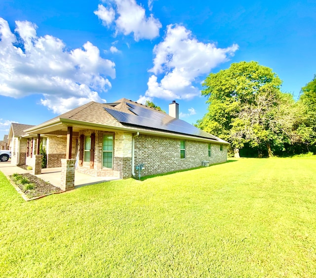 1113 Chesterfield Dr, Webb City, MO 64870 - back of property featuring brick siding, a lawn, solar panels, a patio area, and a chimney
