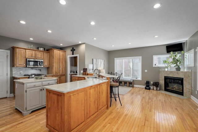 3931 E Stanford St, Springfield, MO 65809 - kitchen featuring stainless steel appliances, a large island with sink, light wood-type flooring, decorative backsplash, and a kitchen bar
