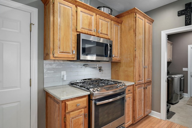 3931 E Stanford St, Springfield, MO 65809 - kitchen with stainless steel appliances, washing machine and clothes dryer, decorative backsplash, brown cabinets, and light wood-type flooring