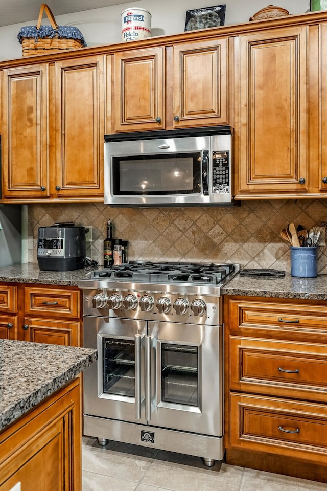 2419 W Deerbrooke Trl, Ozark, MO 65721 - kitchen with stainless steel appliances, brown cabinetry, light tile patterned flooring, stone countertops, and backsplash