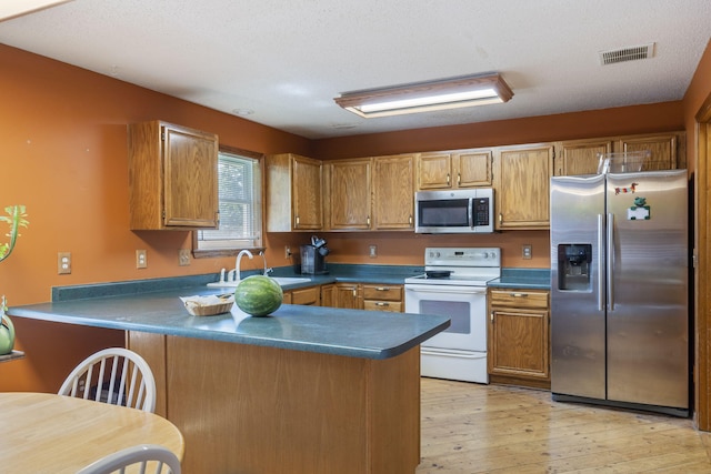508 N Cherry Cir, Nixa, MO 65714 - kitchen featuring stainless steel appliances, a peninsula, dark countertops, light wood-type flooring, and brown cabinets