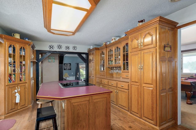 1343 Woodlawn Ave, Mount Vernon, MO 65712 - kitchen featuring black cooktop, a textured ceiling, light wood finished floors, a center island, and glass insert cabinets