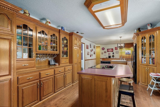 1343 Woodlawn Ave, Mount Vernon, MO 65712 - kitchen featuring a textured ceiling, a kitchen island, brown cabinets, black electric stovetop, and light wood-style floors
