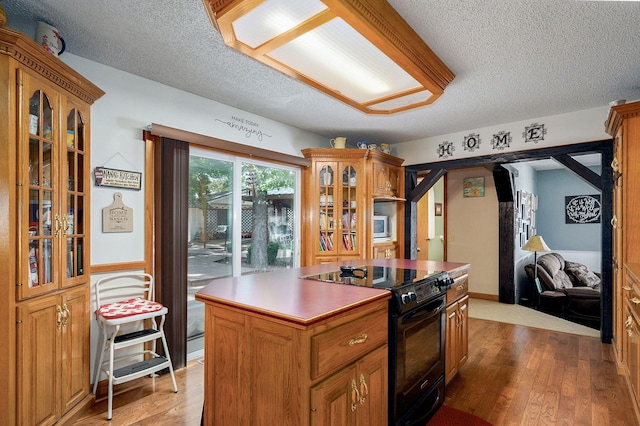 1343 Woodlawn Ave, Mount Vernon, MO 65712 - kitchen featuring black range with electric stovetop, a kitchen island, a textured ceiling, glass insert cabinets, and light wood finished floors