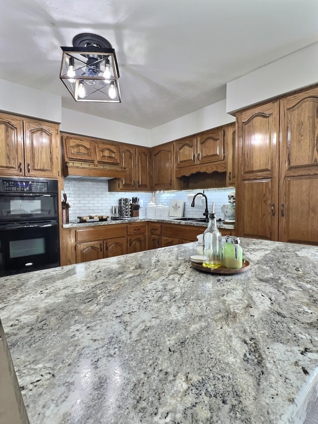 18189 2nd St, Eminence, MO 65466 - kitchen featuring light stone countertops, decorative backsplash, black appliances, custom exhaust hood, and brown cabinets