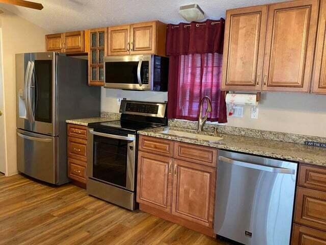 203 Forest Park Ln, Branson, MO 65616 - kitchen featuring appliances with stainless steel finishes, brown cabinetry, light wood finished floors, glass insert cabinets, and a ceiling fan