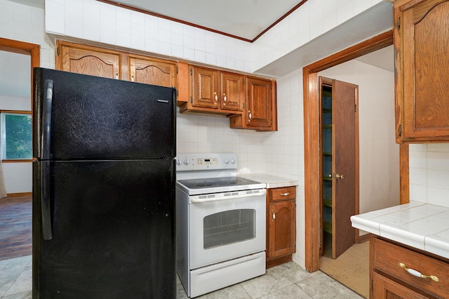225 S Main St, Greenfield, MO 65661 - kitchen featuring freestanding refrigerator, electric range, decorative backsplash, brown cabinetry, and tile counters