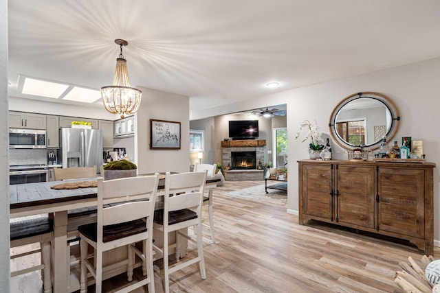 348 Sunset Cv Unit 413, Branson, MO 65616 - dining space featuring a stone fireplace, light wood-style flooring, a chandelier, and ceiling fan