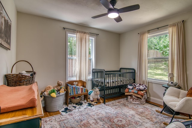 135 Roark Ave, Branson, MO 65616 - bedroom featuring wood finished floors, multiple windows, a nursery area, and a ceiling fan