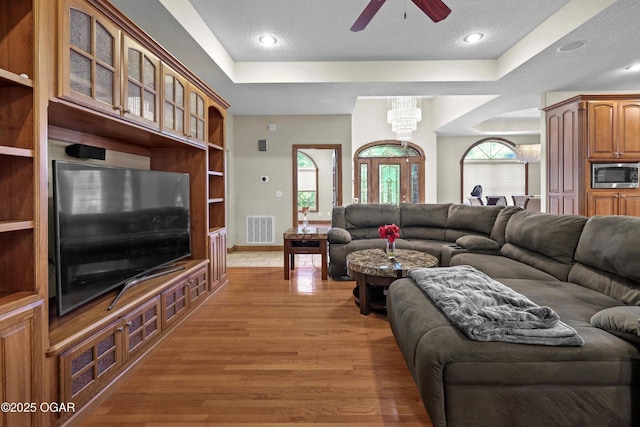 318 Fox Fire Ct, Joplin, MO 64801 - living room featuring a raised ceiling, ceiling fan, light wood-type flooring, a chandelier, and a textured ceiling